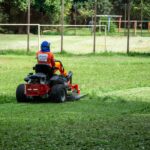 Individual operating a riding lawnmower on a grassy field in a recreational park, Londrina, Brazil.
